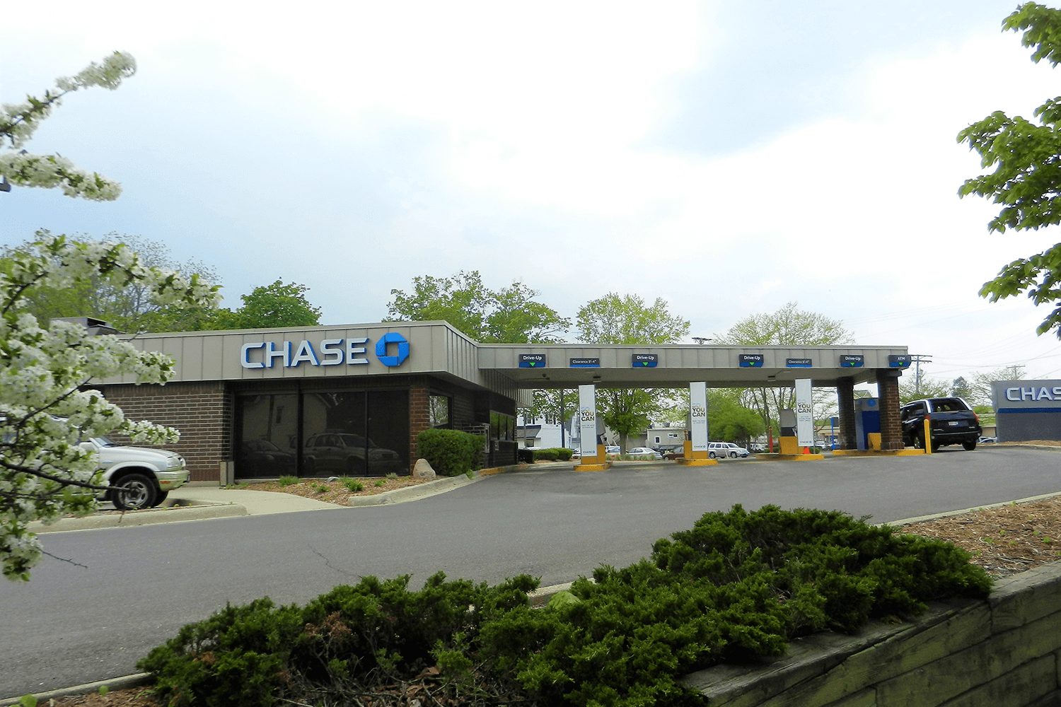 Chase bank branch and drive-thru lanes in a parking lot with trees and a cloudy sky
