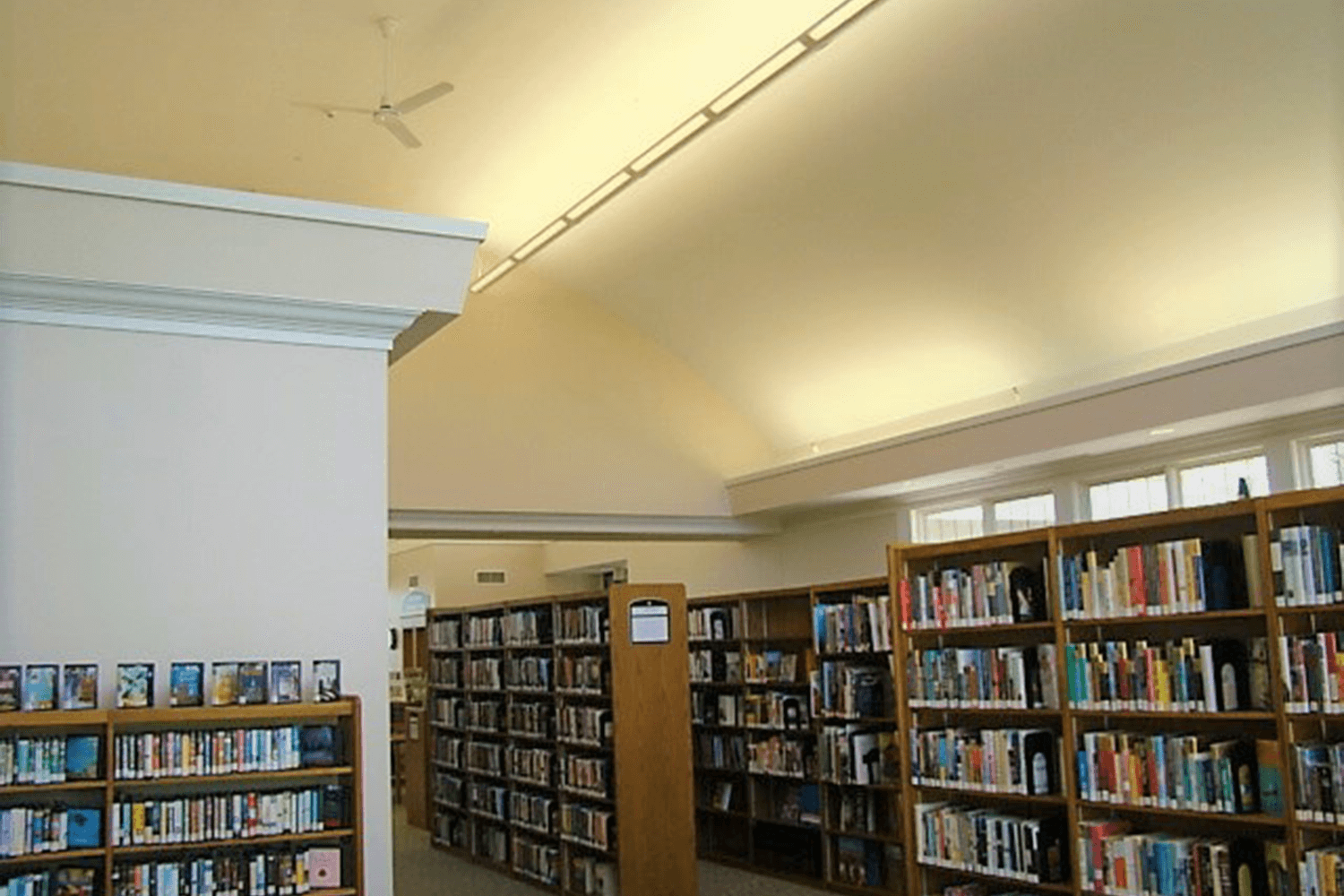 Library interior with tall bookshelves under a vaulted beige ceiling and white walls
