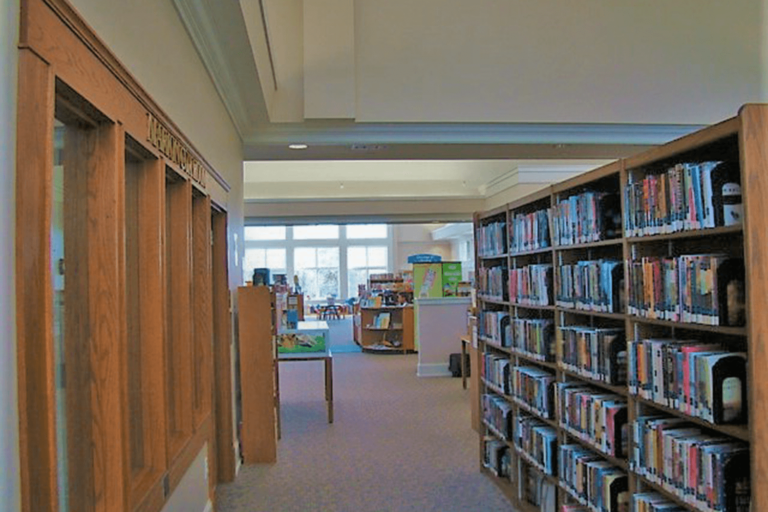 Library aisle with bookshelves and a view into a bright reading area
