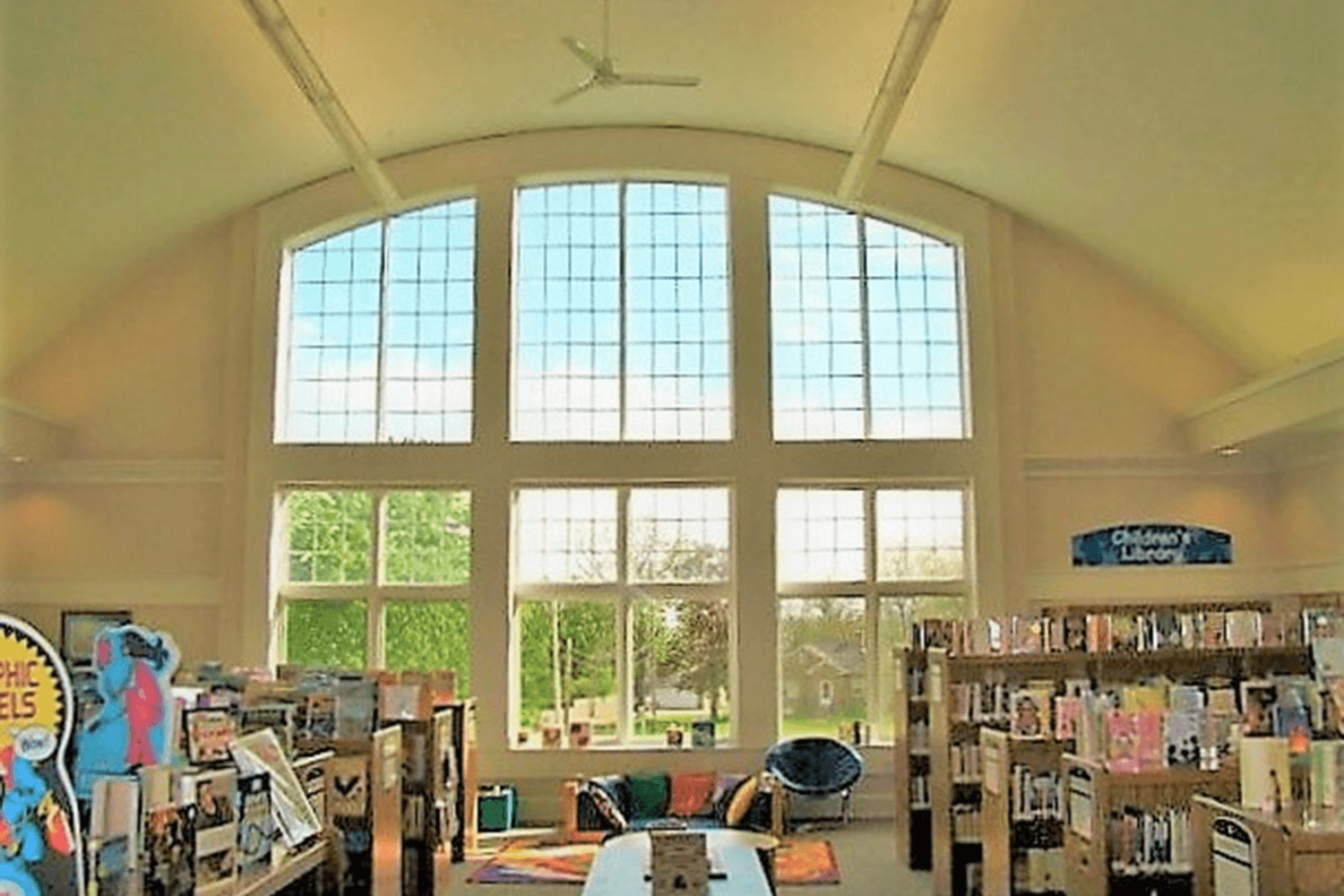 Bright library interior with arched ceiling, large windows, and bookshelves lining both sides.