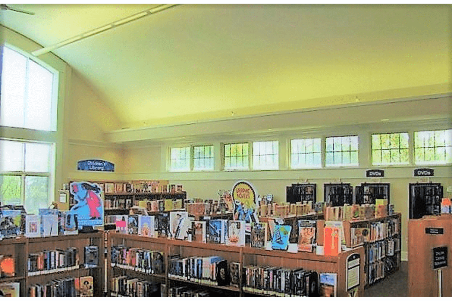 Bright library interior with bookshelves, large windows, and high vaulted ceiling