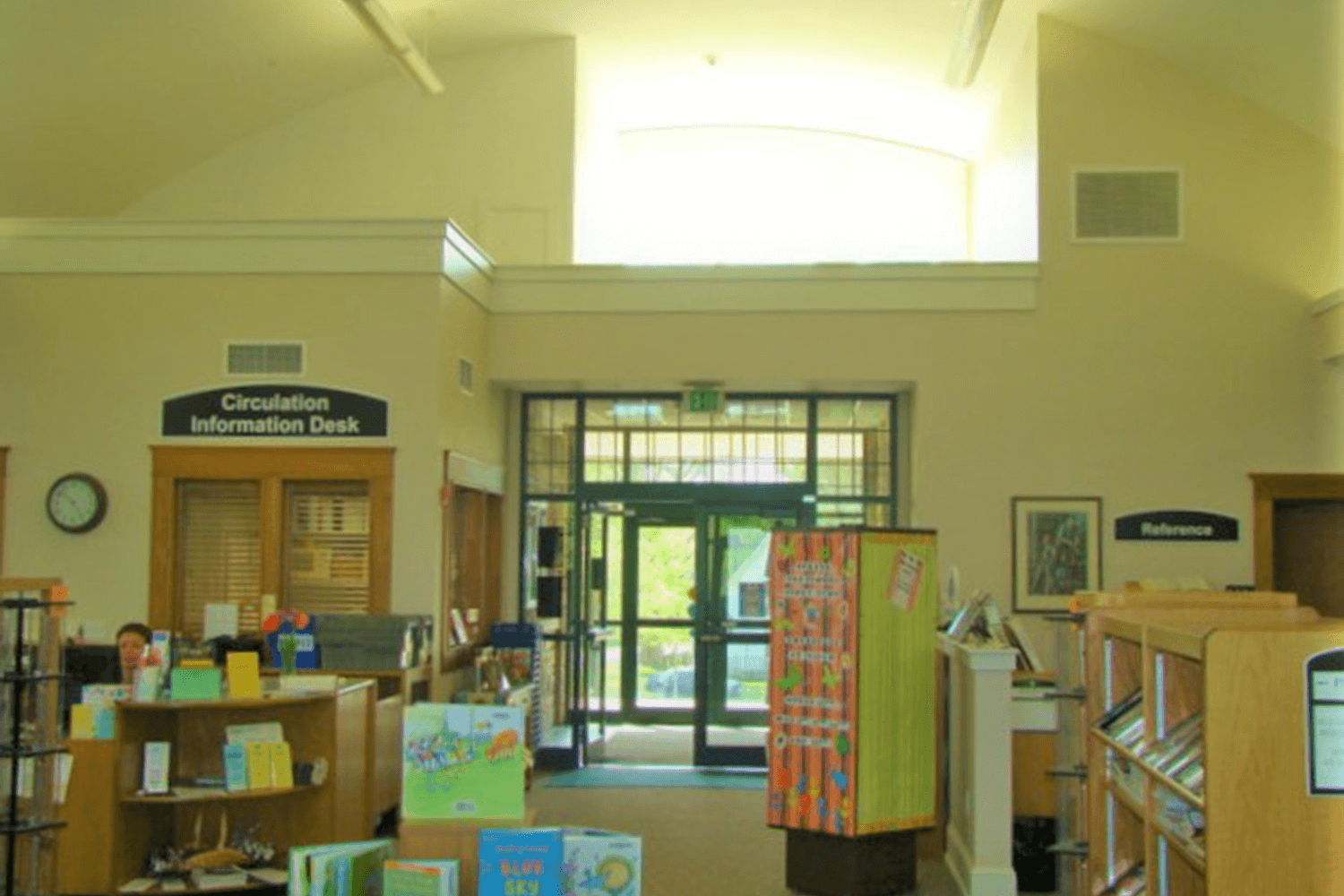 Library or information center interior with bookshelves, posters, and a glass entrance in back.