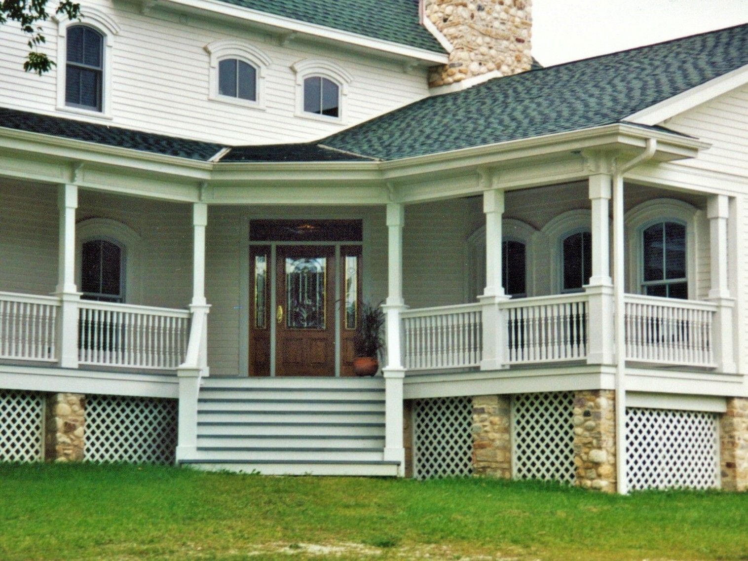 Front porch of a white house with green roof, wooden front door, and white railings with steps leading up.