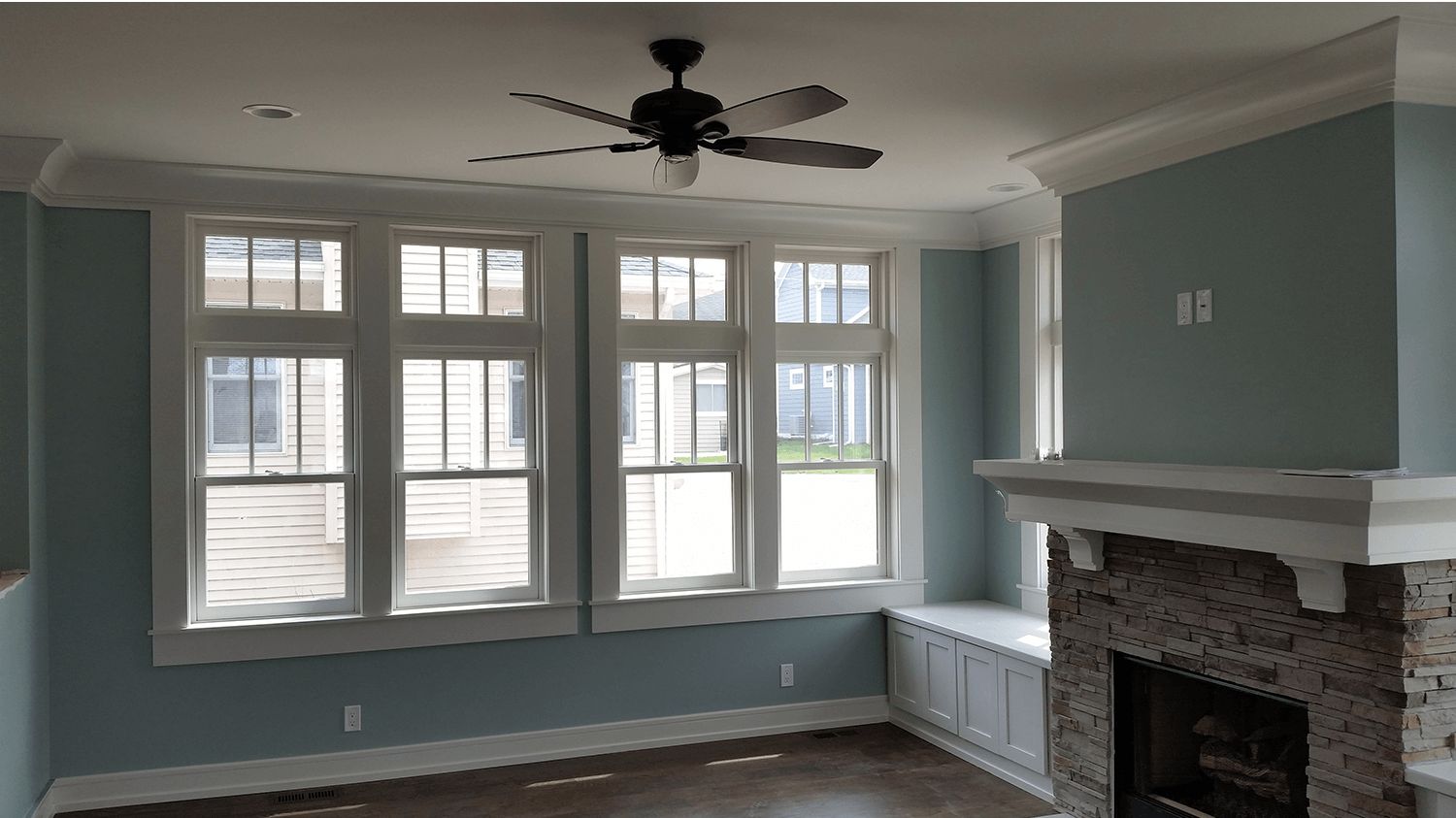 Living room with blue-gray walls, large windows, a ceiling fan, and a brick fireplace