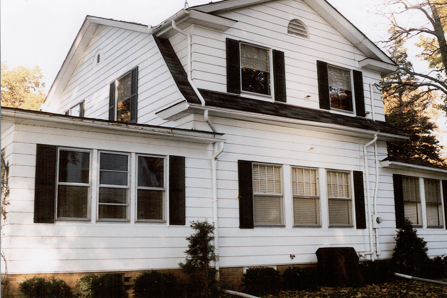 White two-story house with dark shutters and many windows, viewed from the front yard.