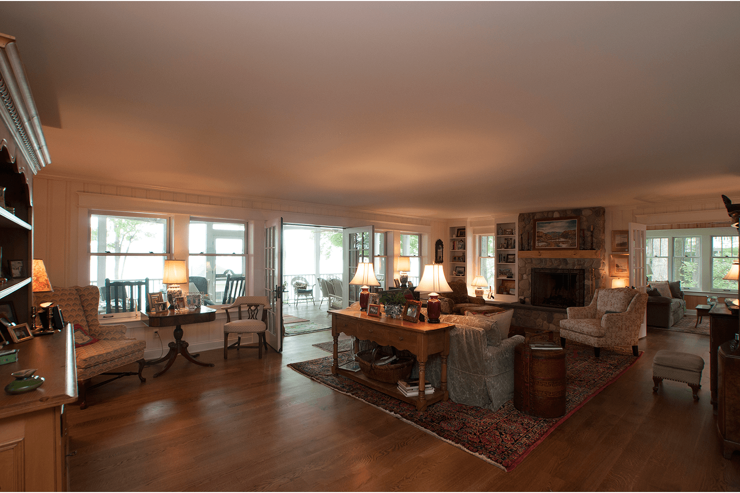 Bright living room with hardwood floors, large windows, couches, fireplace, and a wooden dining table