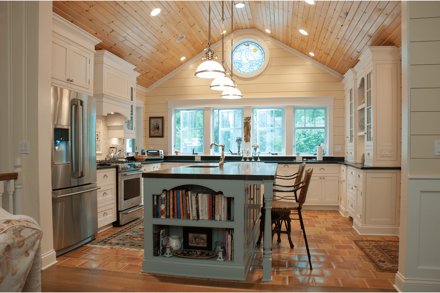Bright kitchen with vaulted wood ceiling, island, stainless fridge, and large window over the sink.