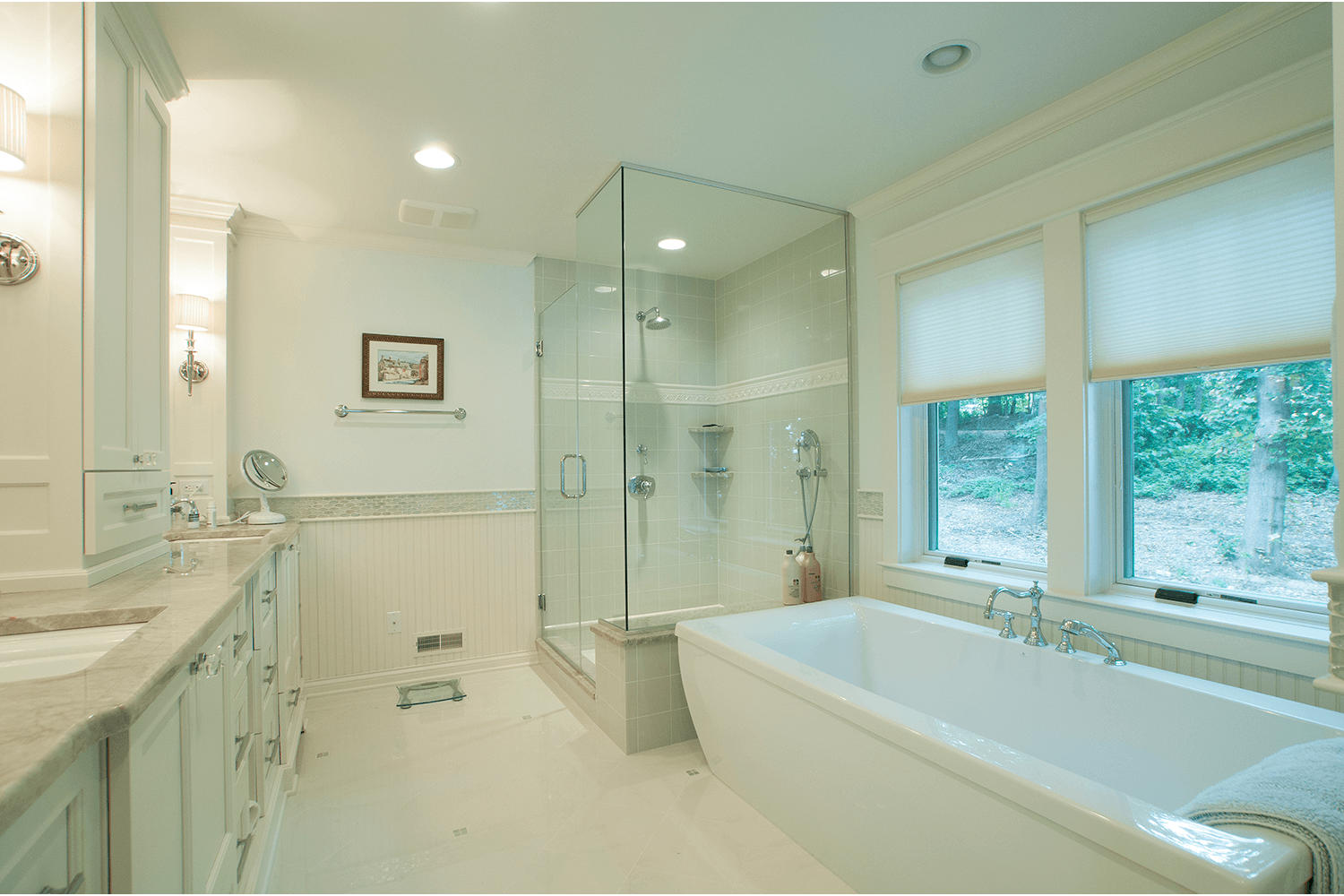Bright white bathroom with a double vanity, bathtub, glass shower, and large window.