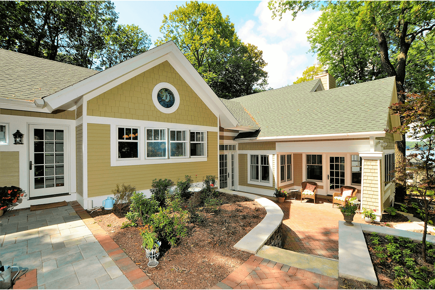 Tan house with green roof, white trim, and landscaped front courtyard on a sunny day