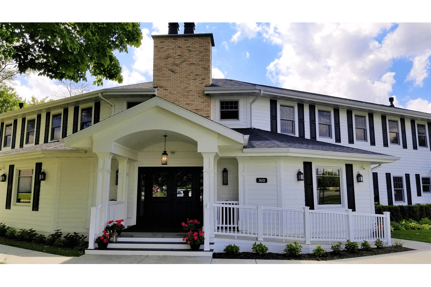 White two-story house with wraparound porch and central brick chimney under a partly cloudy sky