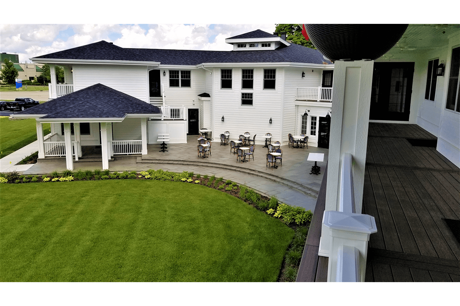 White two-story building with a lawn, gazebo, and patio chairs, viewed from a covered walkway
