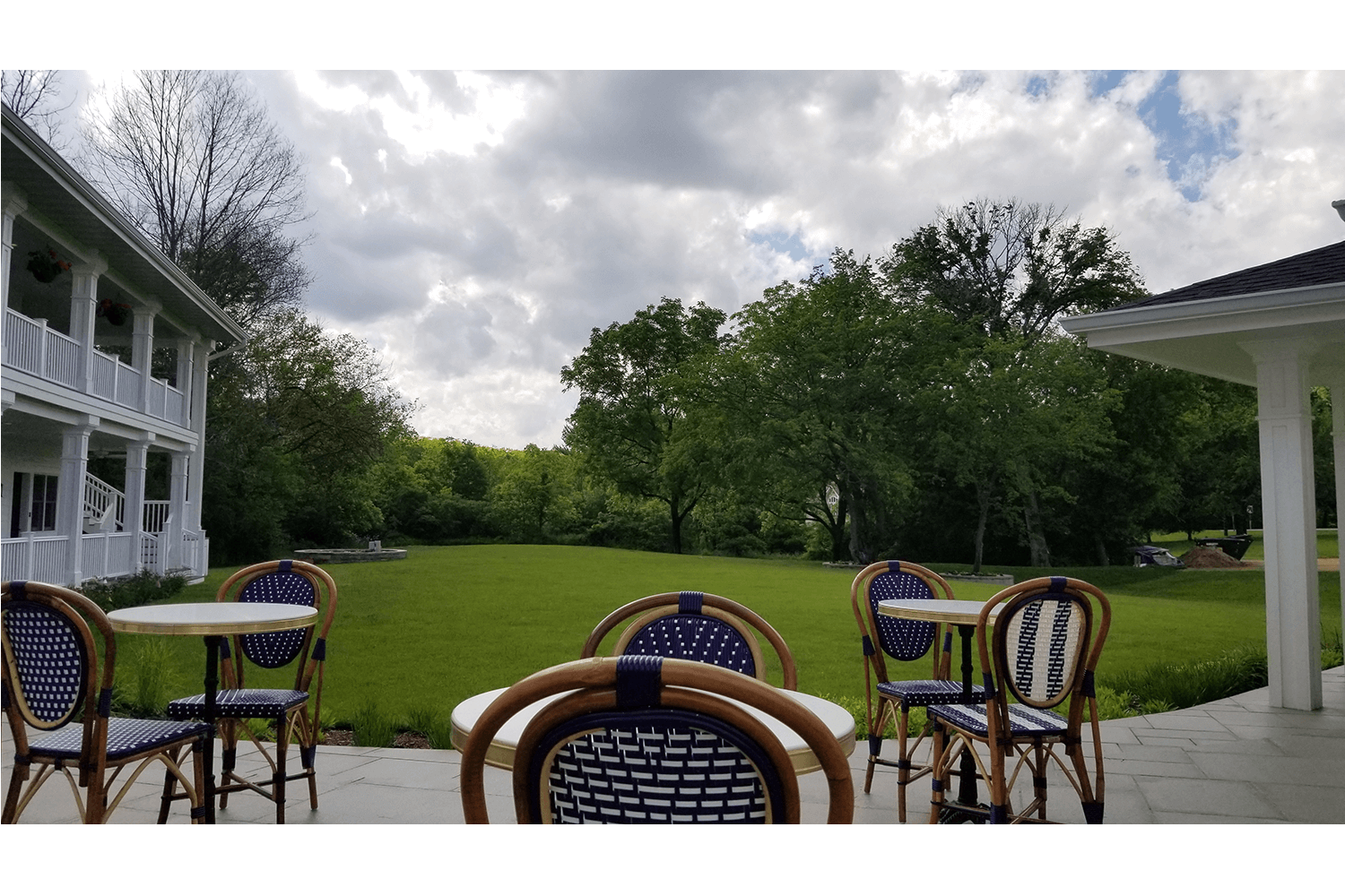 Outdoor patio with blue wicker chairs overlooking a green lawn and cloudy sky