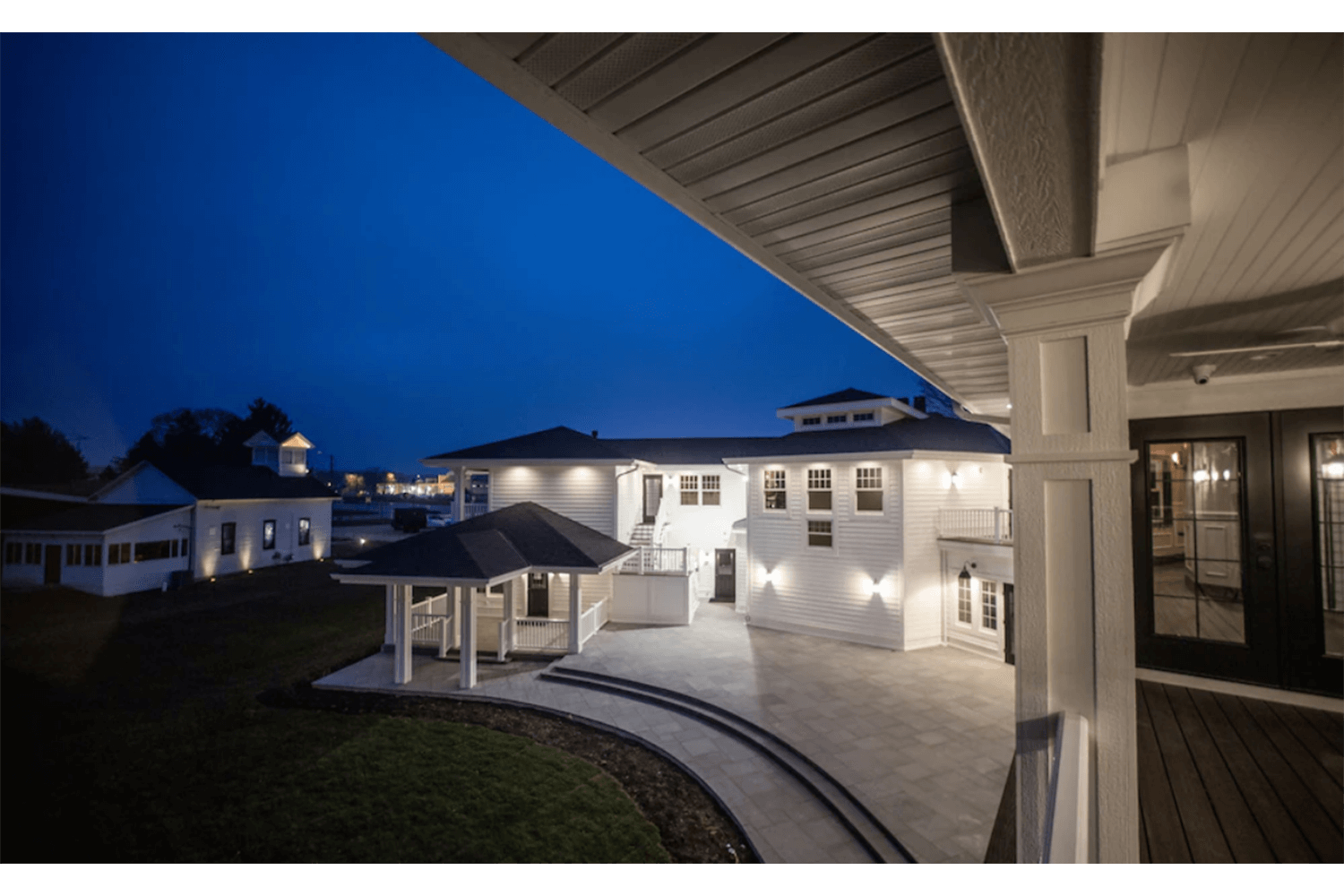 Night view of a large white house with lit windows and a curved walkway under a covered porch