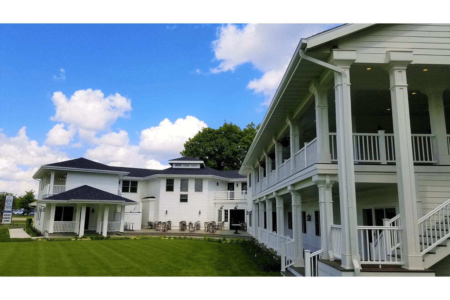 White colonial-style house with porch and columns beside a lawn under a blue sky