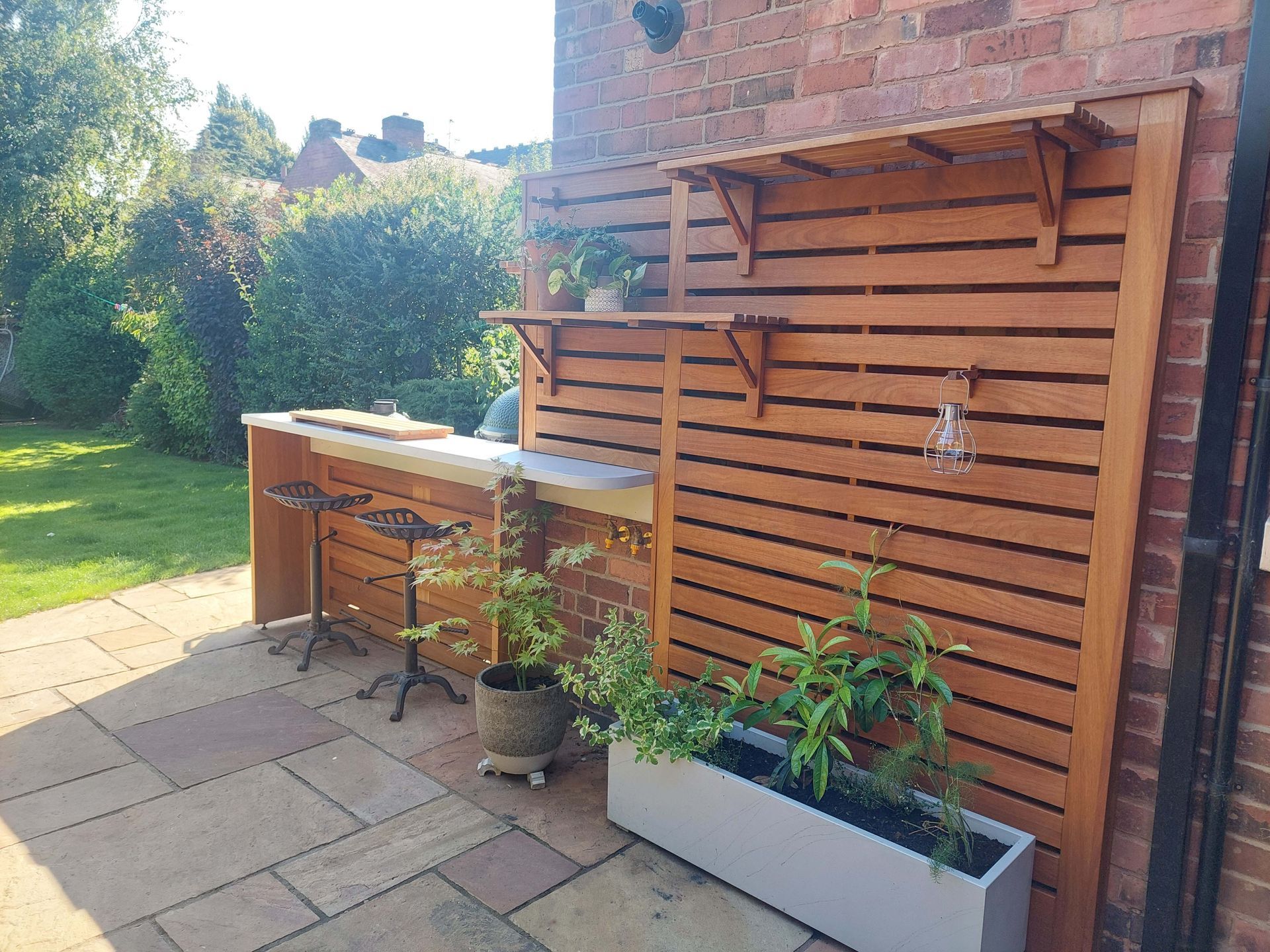 Outdoor patio with wooden slat wall, potted plants, and a built-in sink beside a brick house