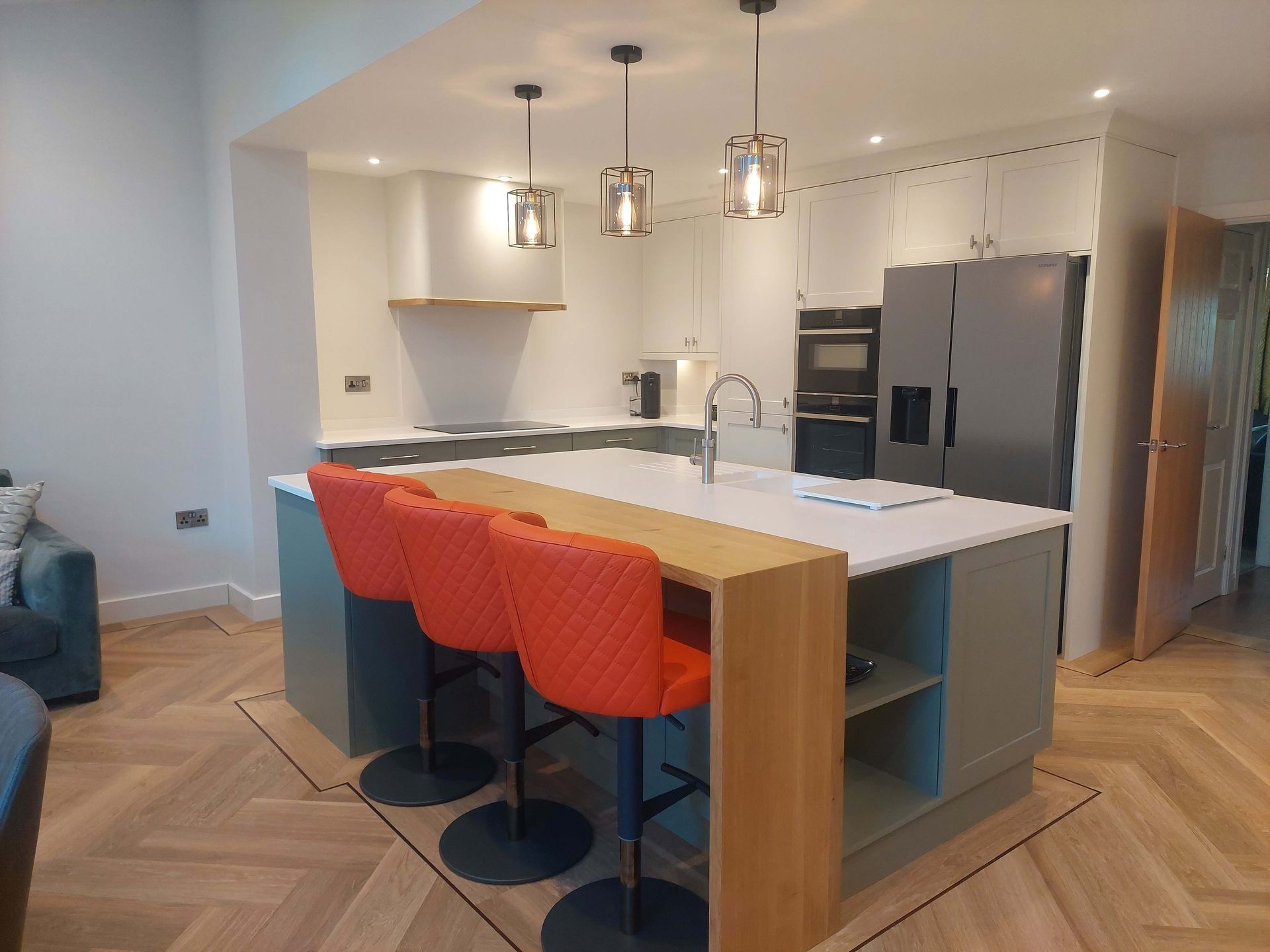 Modern kitchen with island, three orange bar stools, pendant lights, and stainless steel appliances