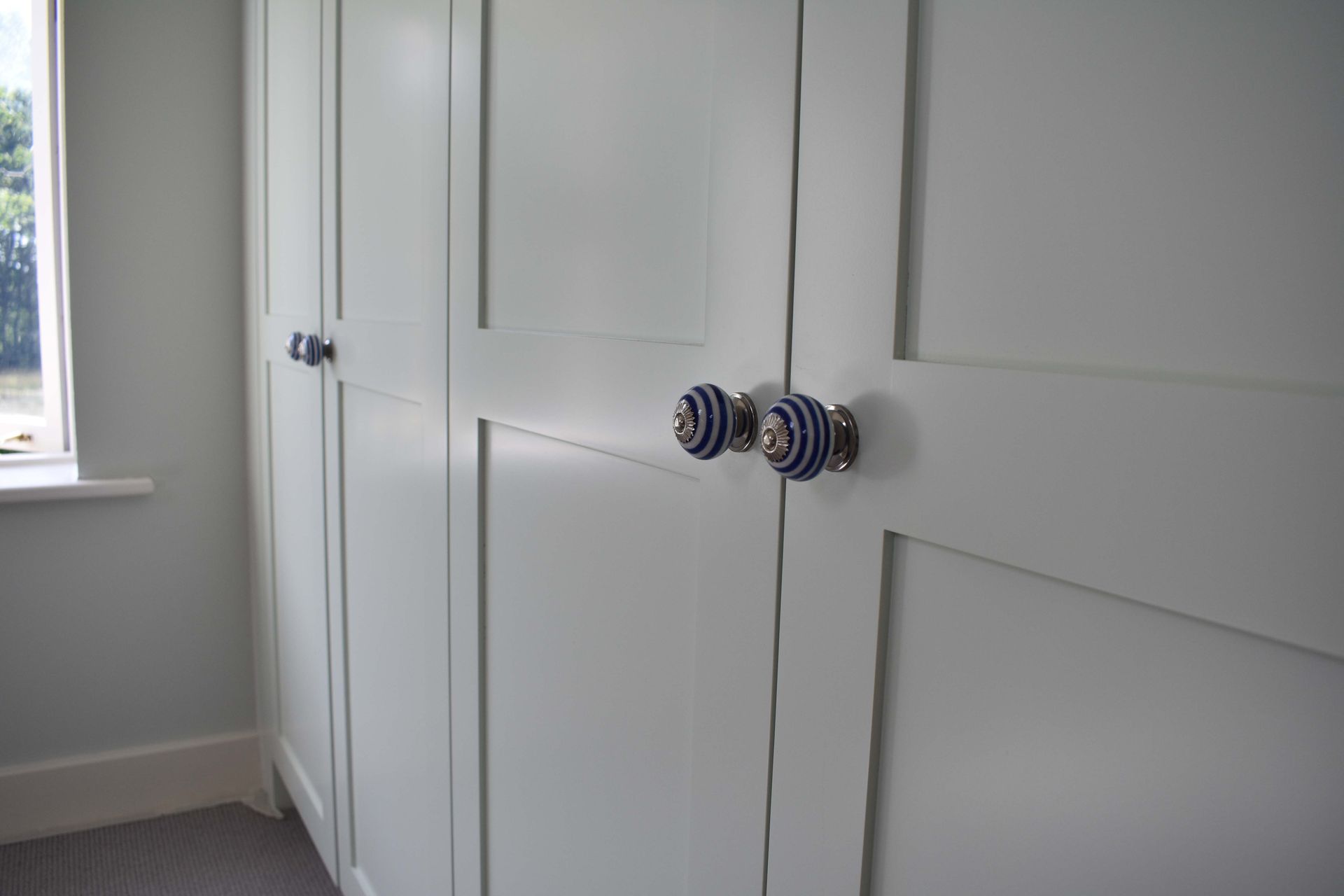 Bedroom closet doors with striped round knobs beside a window