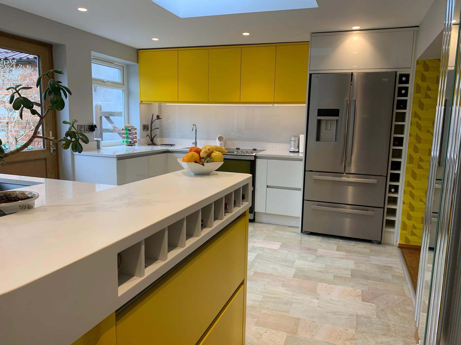 Modern kitchen with bright yellow cabinets, white island, stainless steel fridge, and bowl of fruit.