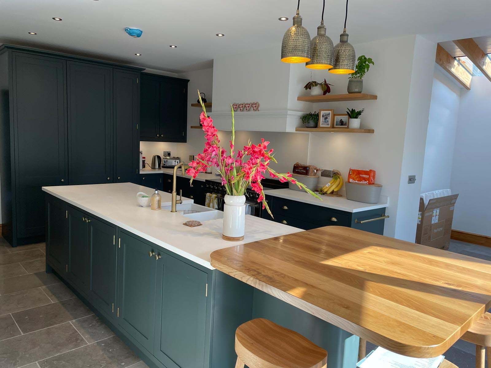 Modern kitchen with dark green cabinets, white island, pendant lights, and flowers on the counter