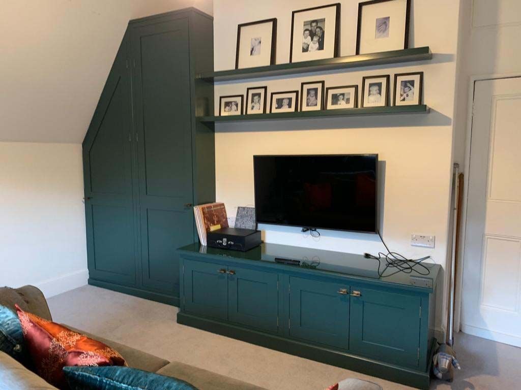 Built-in green cabinets and shelves with framed photos, a TV, and a beige sofa in a bright living room