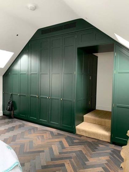 Green paneled built-in wardrobe wall with a doorway and small carpeted step in a sloped-ceiling room