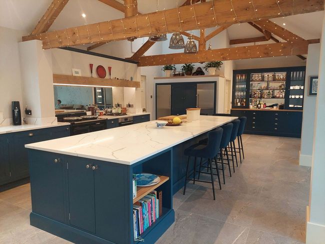 Spacious kitchen with a large white island, dark blue cabinets, exposed wood beams, and stools along the counter
