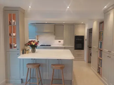 Bright modern kitchen with a white island, two wooden stools, and built-in cabinets.