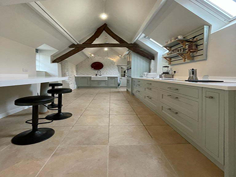 Bright attic kitchen with skylights, beige tile floor, white cabinets, and a small black table and stools.