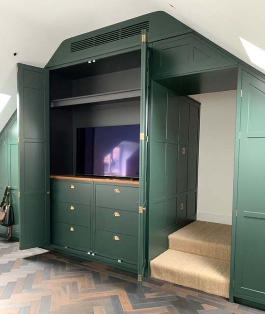 Green built-in wardrobe with drawers, TV niche, and beige carpeted step in a room.