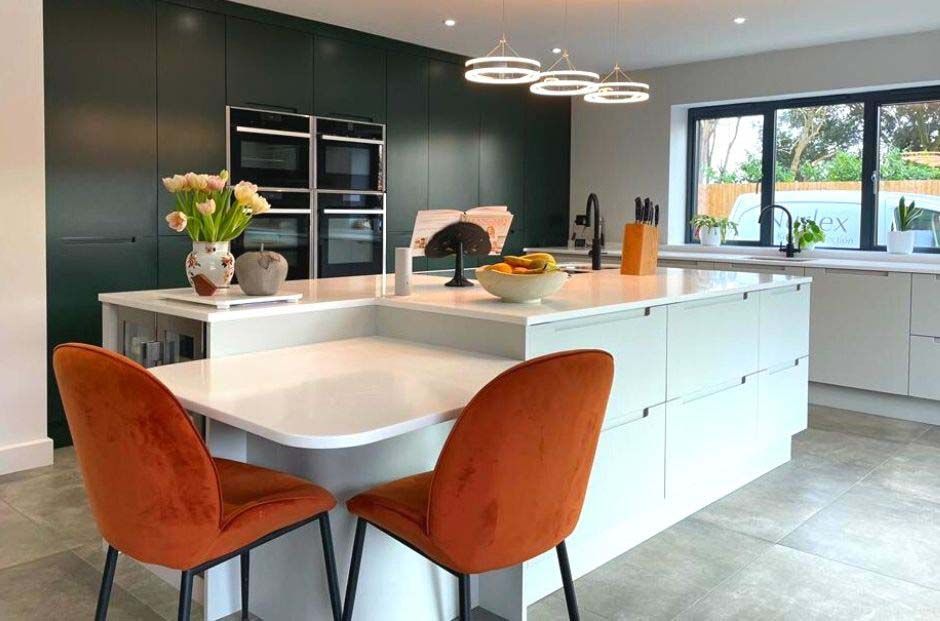 Modern kitchen with white island, orange chairs, dark cabinets, and large windows overlooking greenery