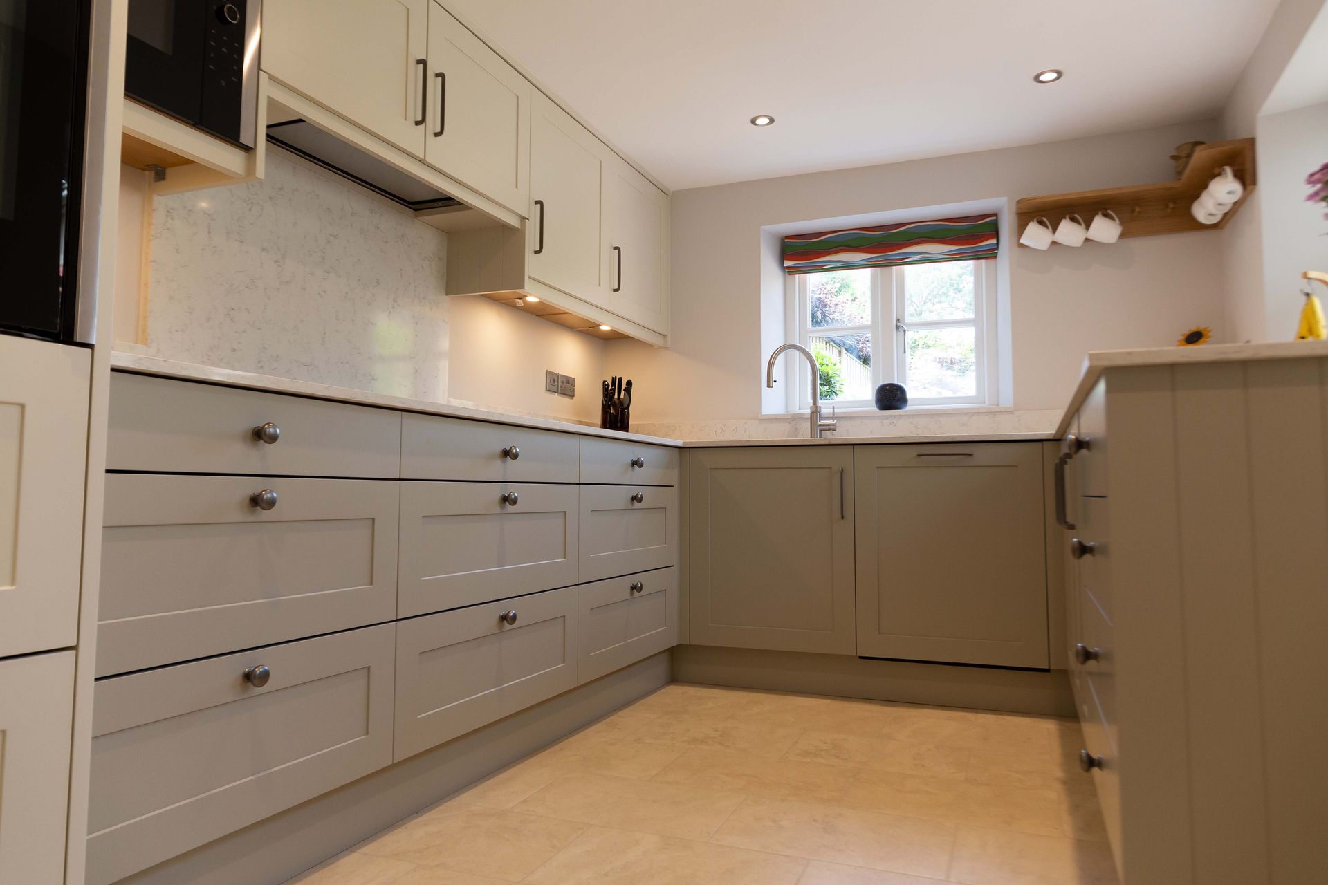 Modern beige kitchen with built-in cabinets, countertop, window, and sink under warm lighting