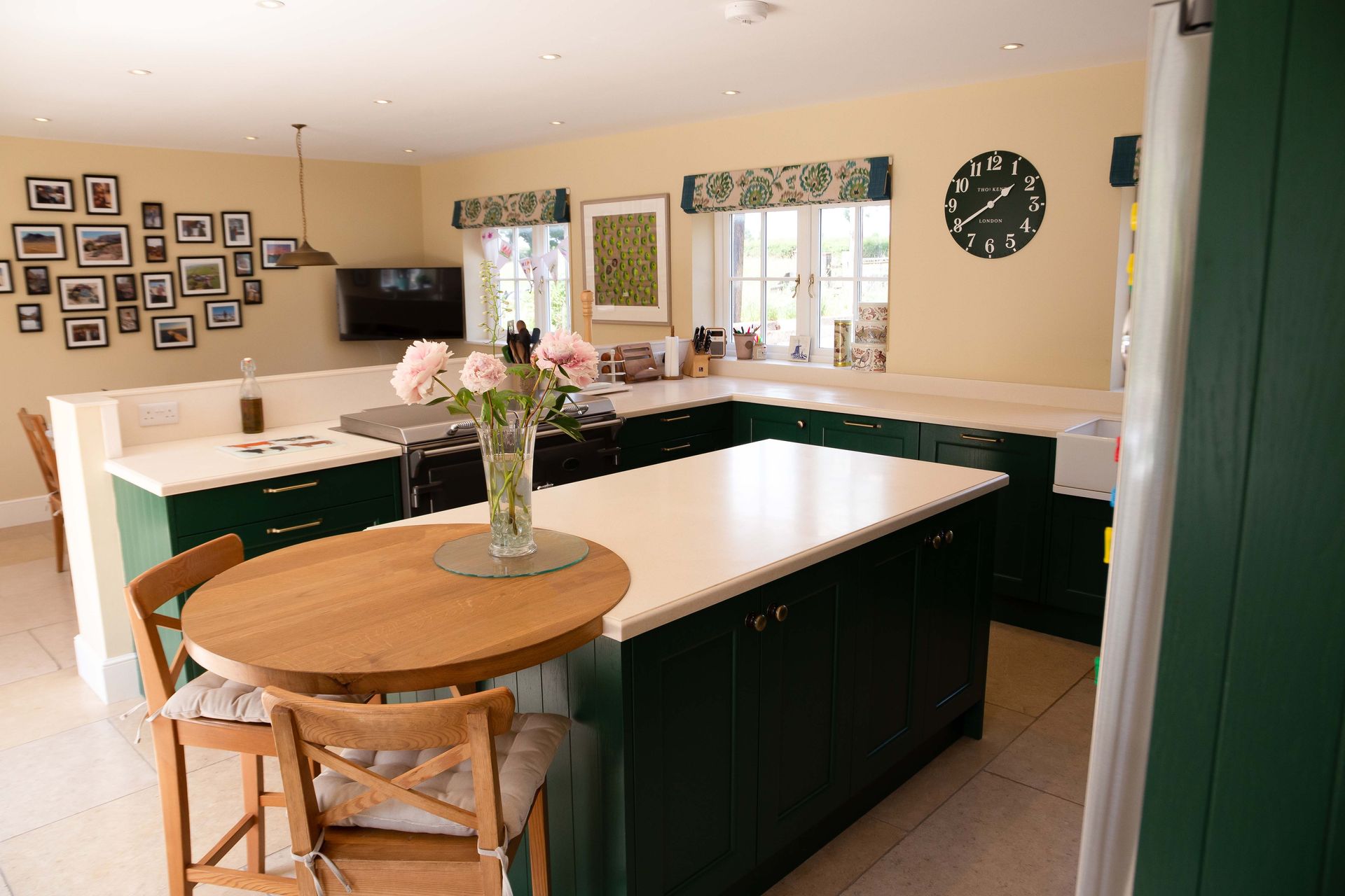 Bright kitchen with white island, dark cabinets, round table, flowers, and wall clock