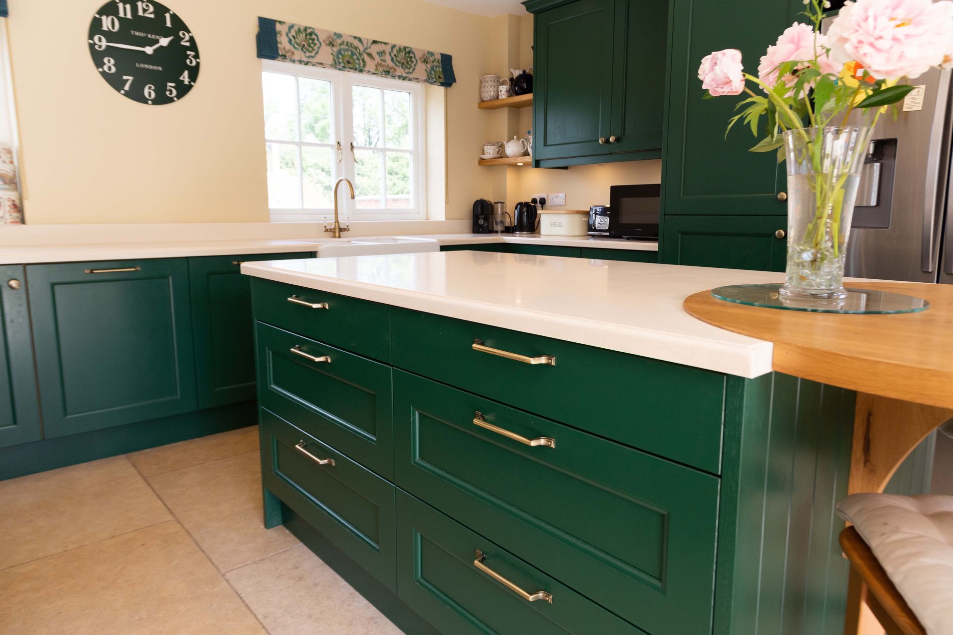 Green kitchen with white countertops, wooden island, and vase of pink flowers by a window