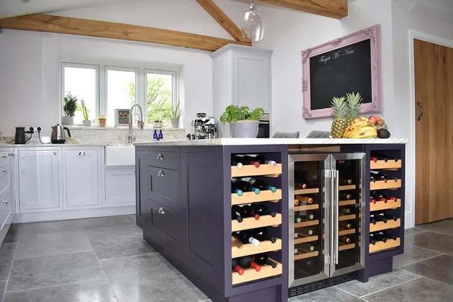 Modern kitchen with gray island, wine racks, white cabinets, and exposed wooden beams