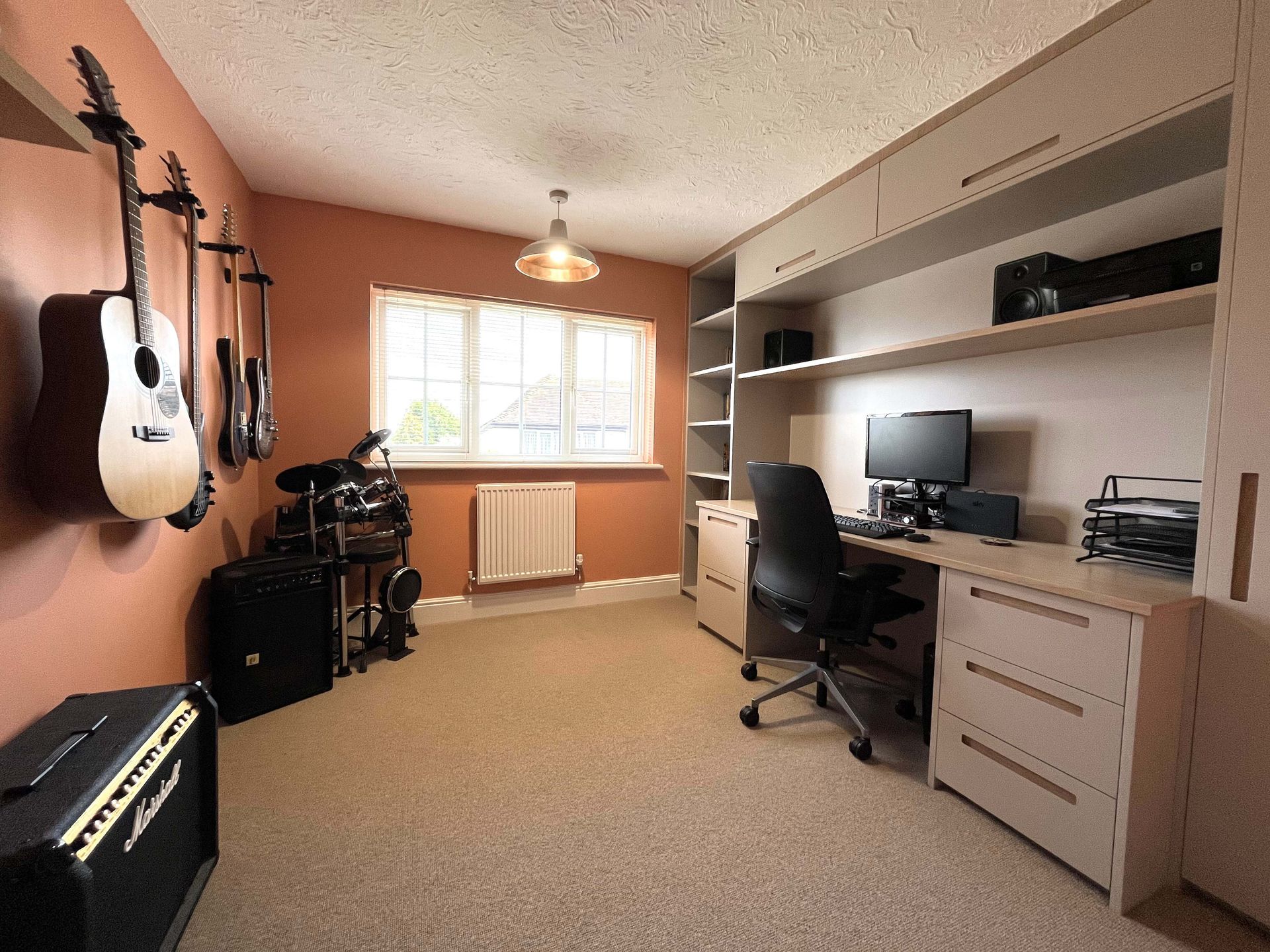Small home office/music room with desk, computer, guitars, and a window with blinds.