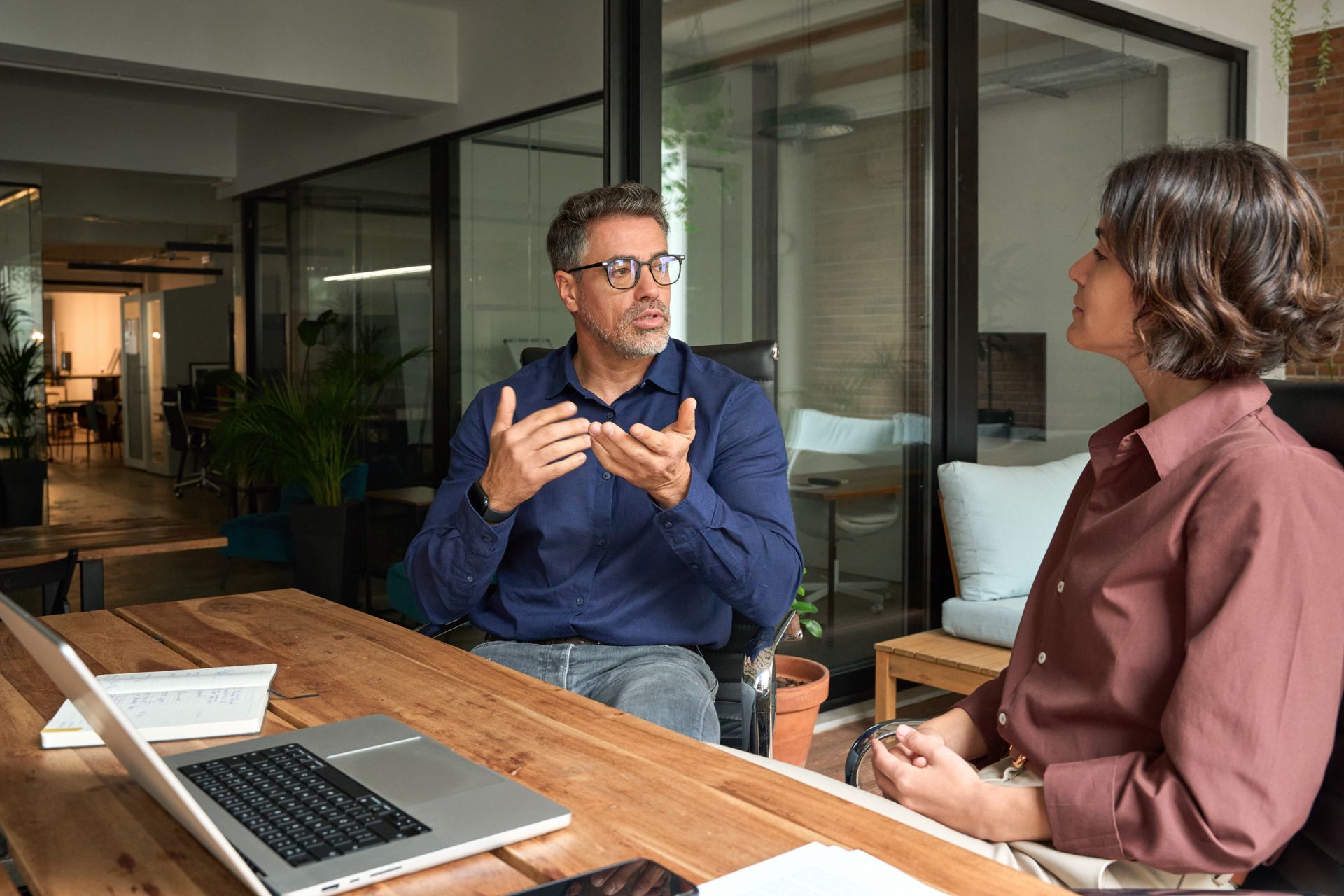 Two people talking in a modern office beside a laptop and wooden table