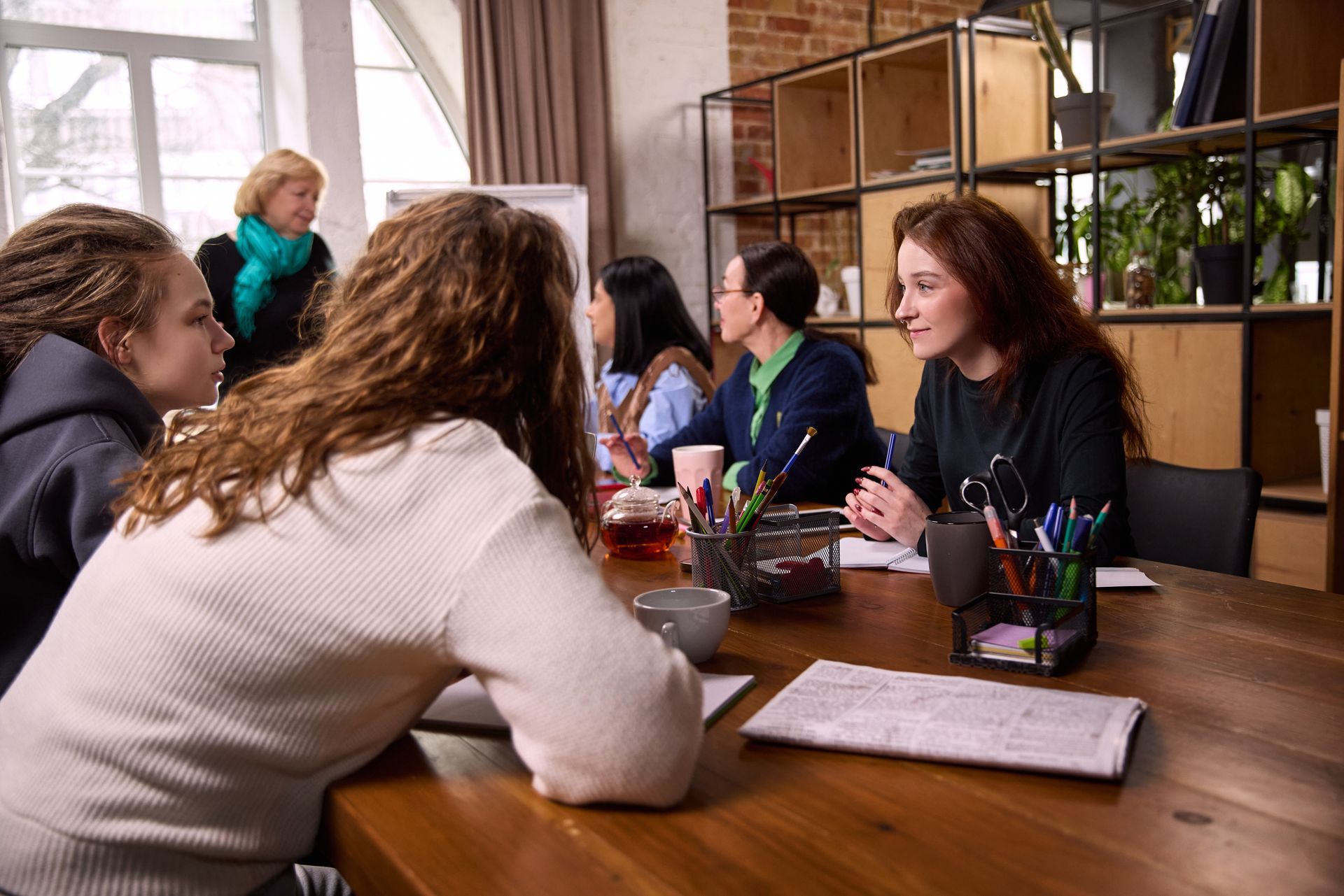 People sitting around a wooden table in a café, talking over coffee and notebooks.