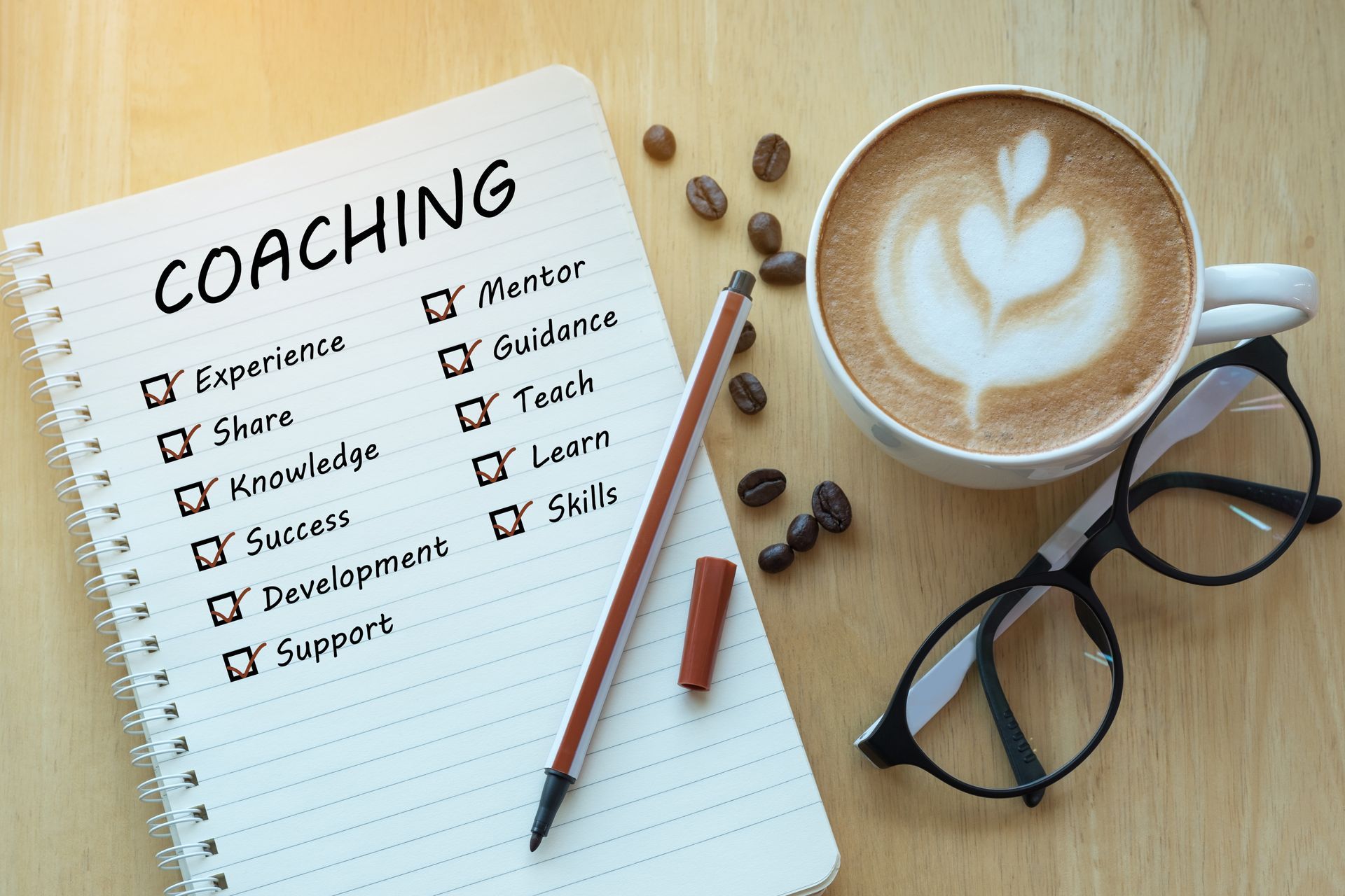 Coaching notebook with checklist beside coffee, glasses, and pencil on a desk