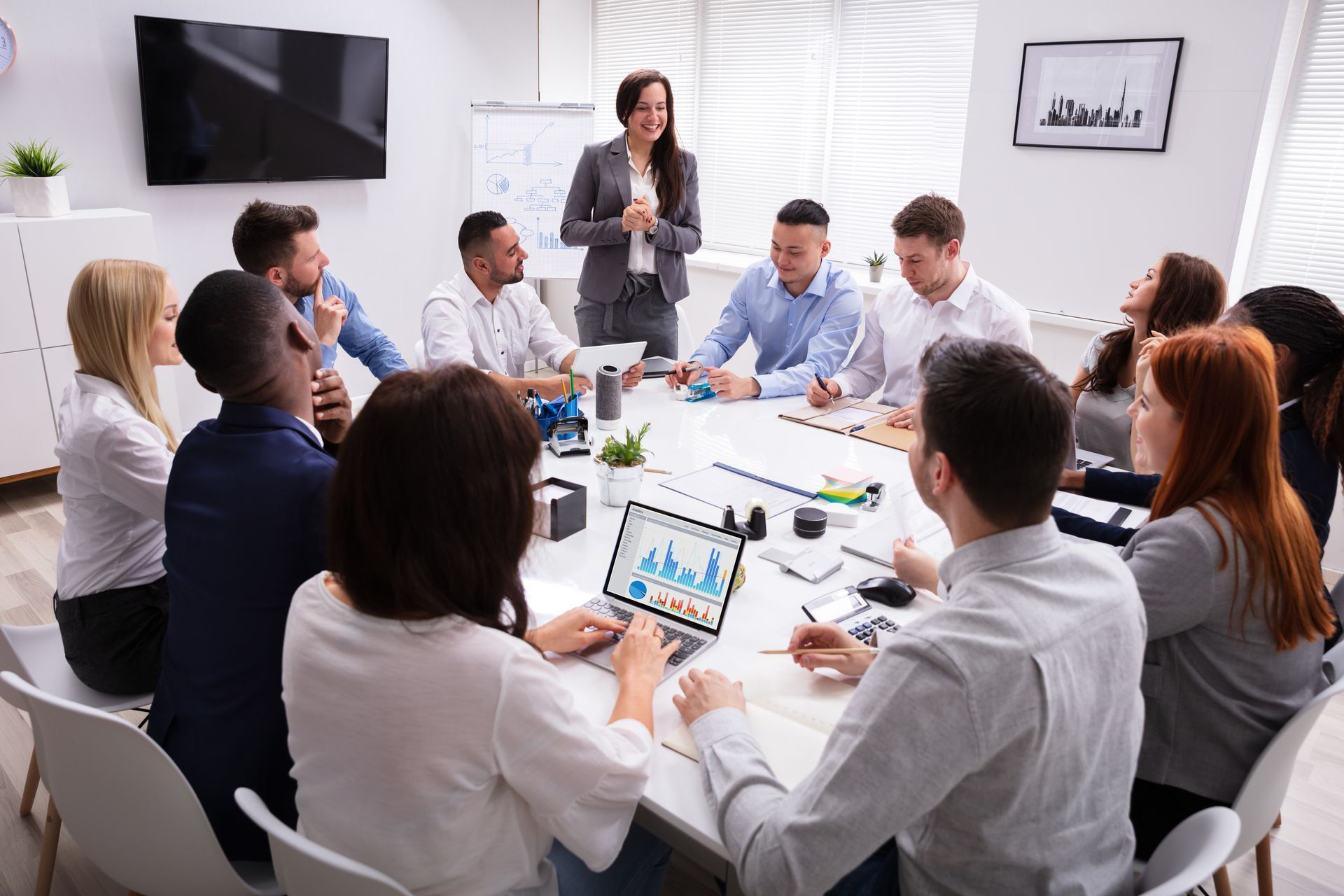 Team meeting in a bright conference room, with a presenter speaking to seated colleagues around a table.
