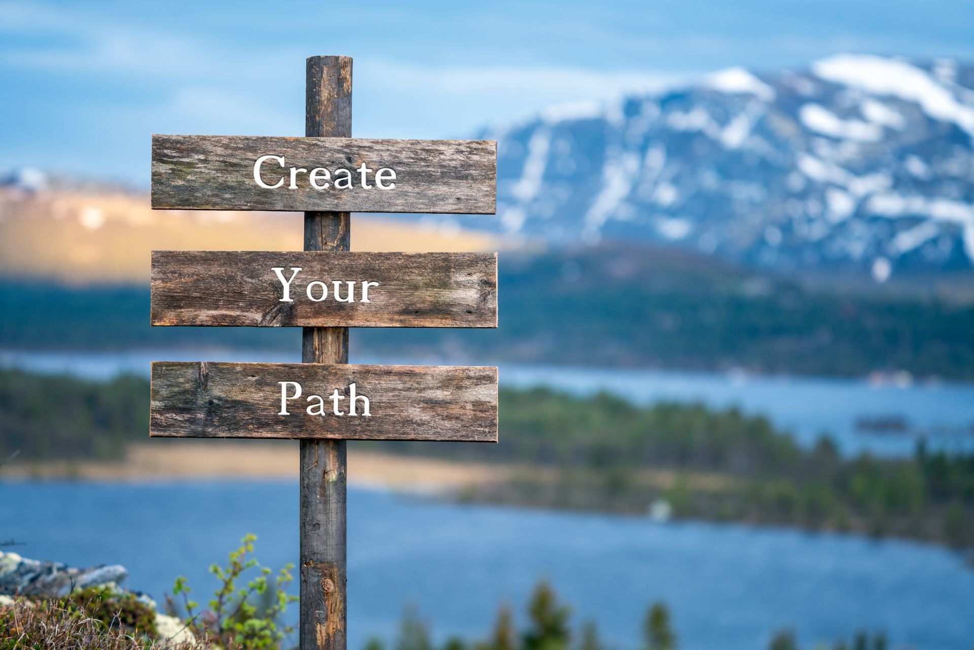 Wooden sign reading “Create Your Path” against a mountain and lake backdrop