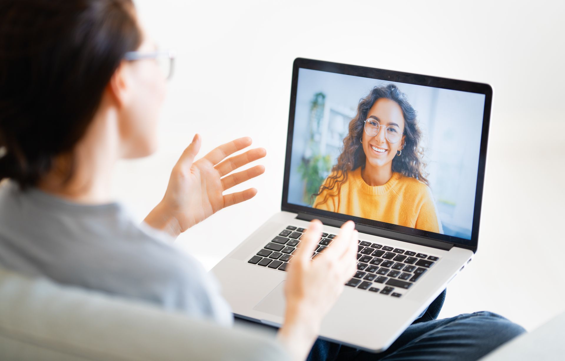 Person having a video call on a laptop, gesturing toward the screen with a smiling caller.