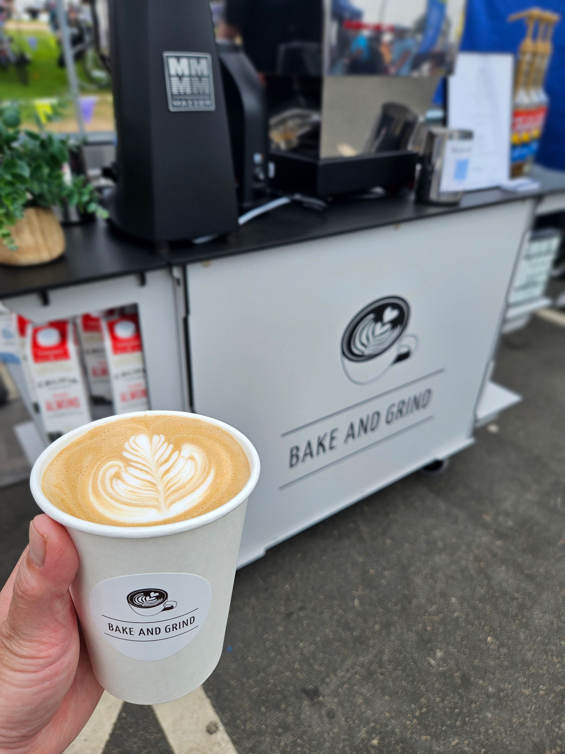 Handcrafted latte in front of the Bake and Grind mobile coffee cart