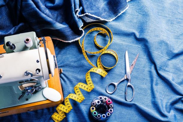 Sewing machine with yellow measuring tape, scissors, and pincushion on blue denim fabric