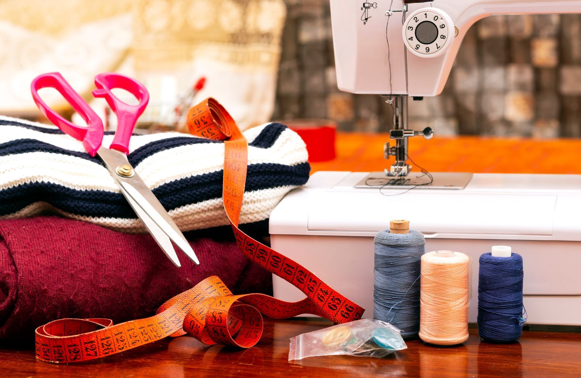 Sewing machine, scissors, ribbon, and thread spools on a table with folded fabric.