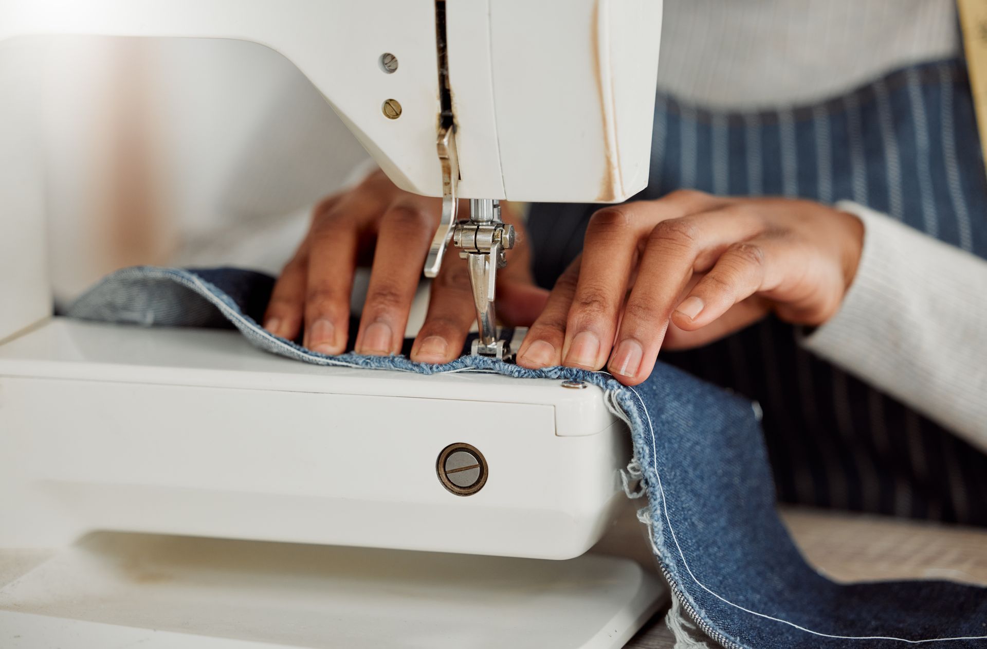 Hands guiding denim under a sewing machine needle while stitching fabric
