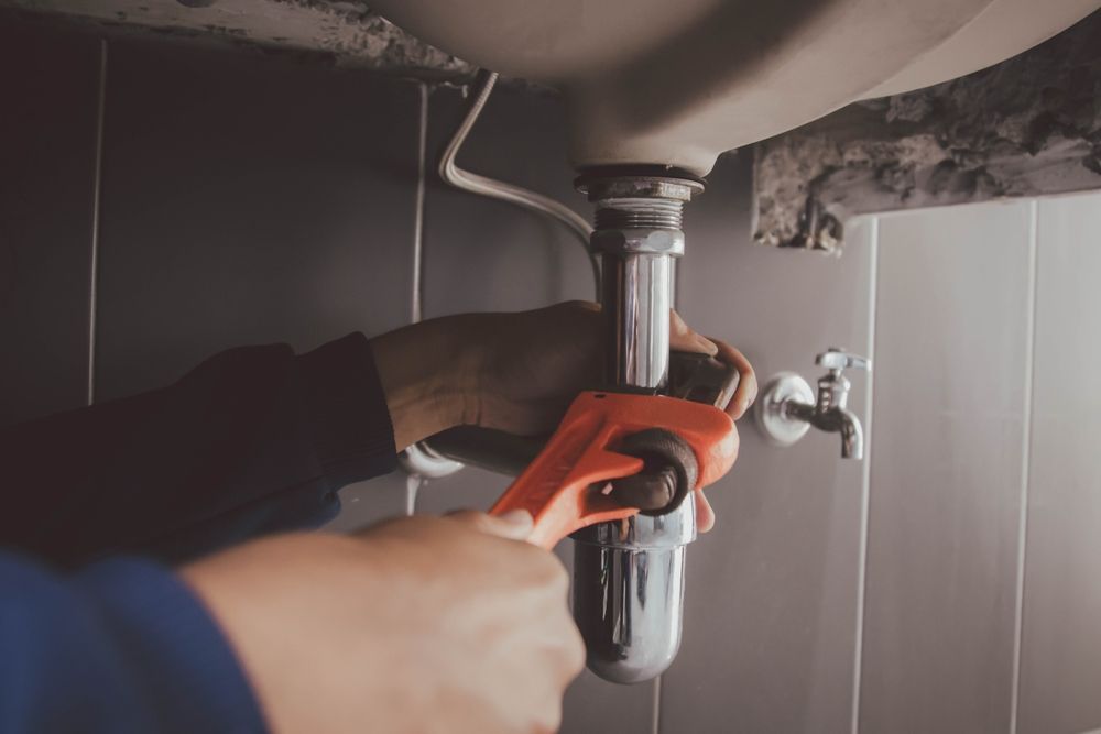 A plumber is fixing a sink pipe with a wrench.