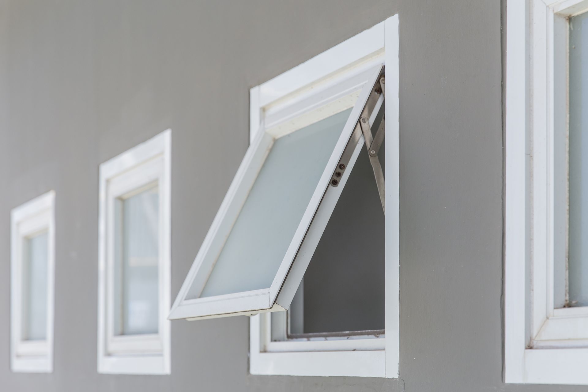 White-framed window, one open to let in air, against gray wall.