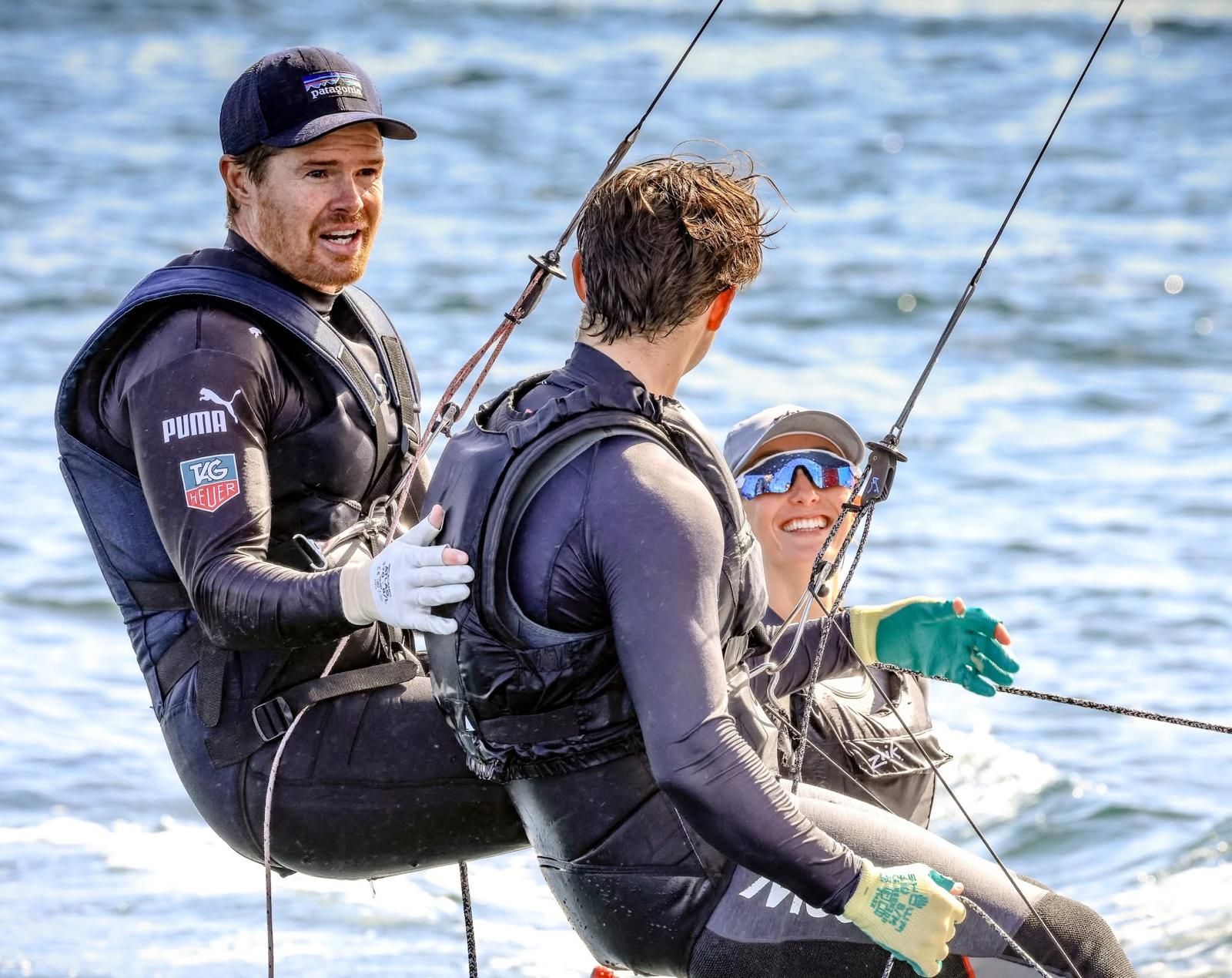 Three sailors in wetsuits on a boat, smiling and adjusting lines on the water — Gosford Sailing Club in Gosford, NSW