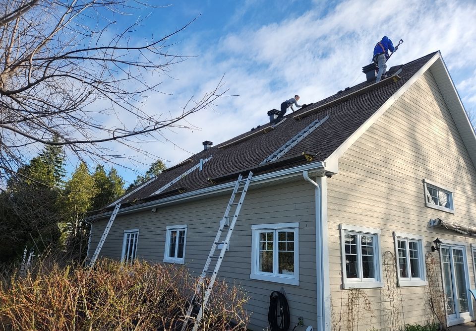 Workers on roof of house, using ladders. Sunny day, blue sky.