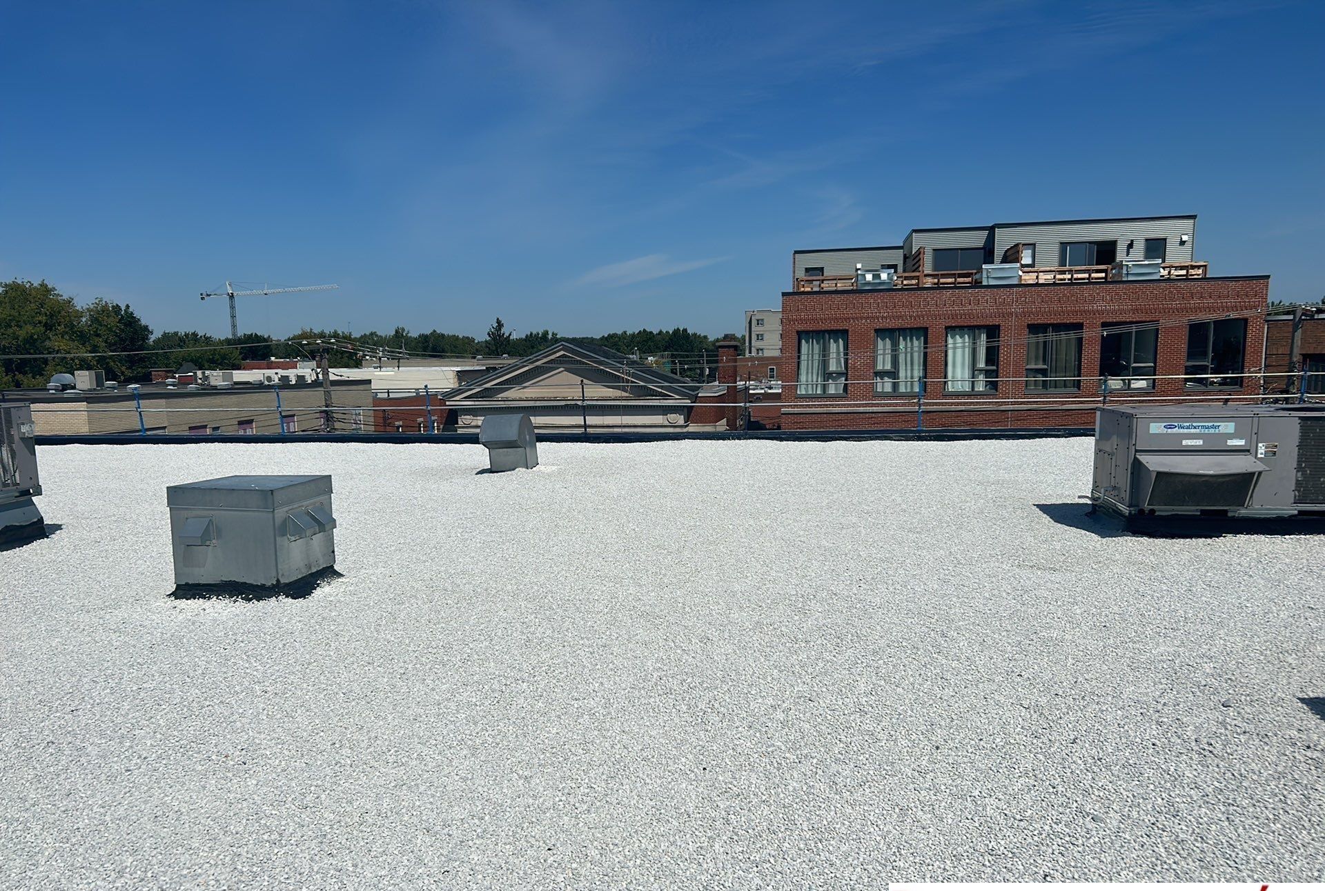 Toit plat recouvert de gravier blanc avec unités CVC ; un bâtiment en briques avec des fenêtres visibles en arrière-plan par une journée ensoleillée.